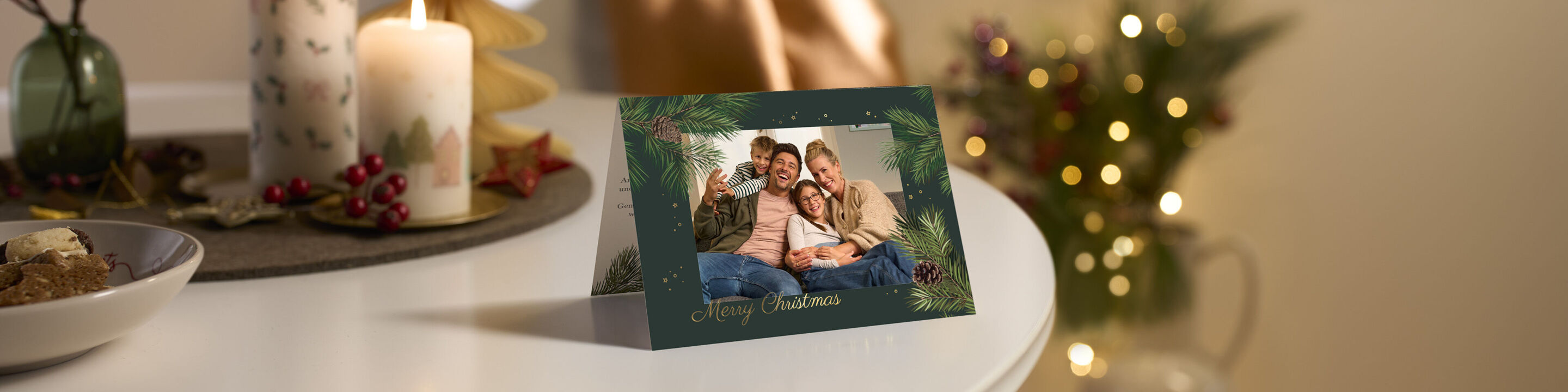 kartka swiateczna CEWE ze zdjeciem rodziny i napisem Merry Christmas postawiona na stole ze swieca w tle rozmyta choinka